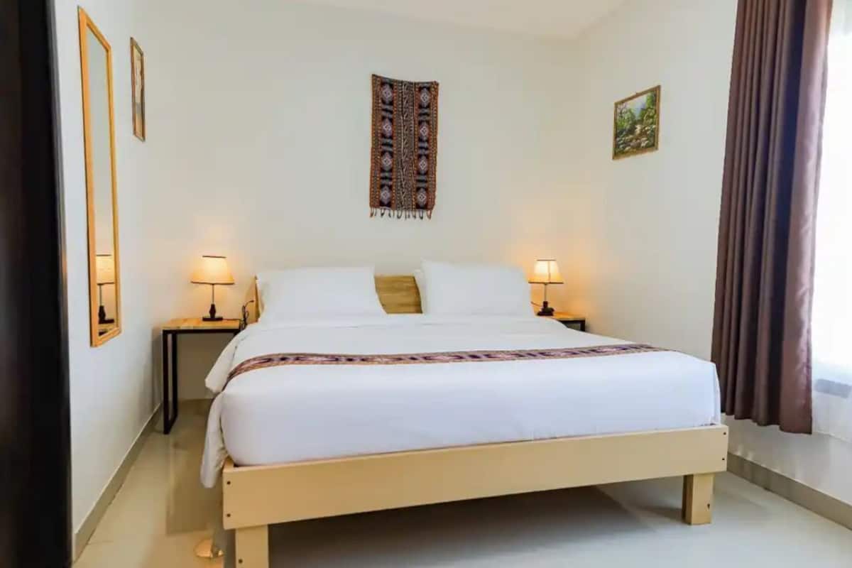 A neatly arranged bedroom with a single bed, two bedside tables, a wall tapestry, and a window with curtains.