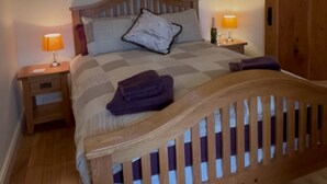 Quarto com cama de madeira, duas mesas de cabeceira com luminárias, guarda-roupa de madeira e um claraboia sobre a cama.