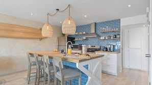 A modern kitchen with a central island, wooden chairs, and a hanging light fixture. - Walk to Trestles Beach, Shared Yard+firepit El Camino Surfhouse A by Avantstay (San Clemente)