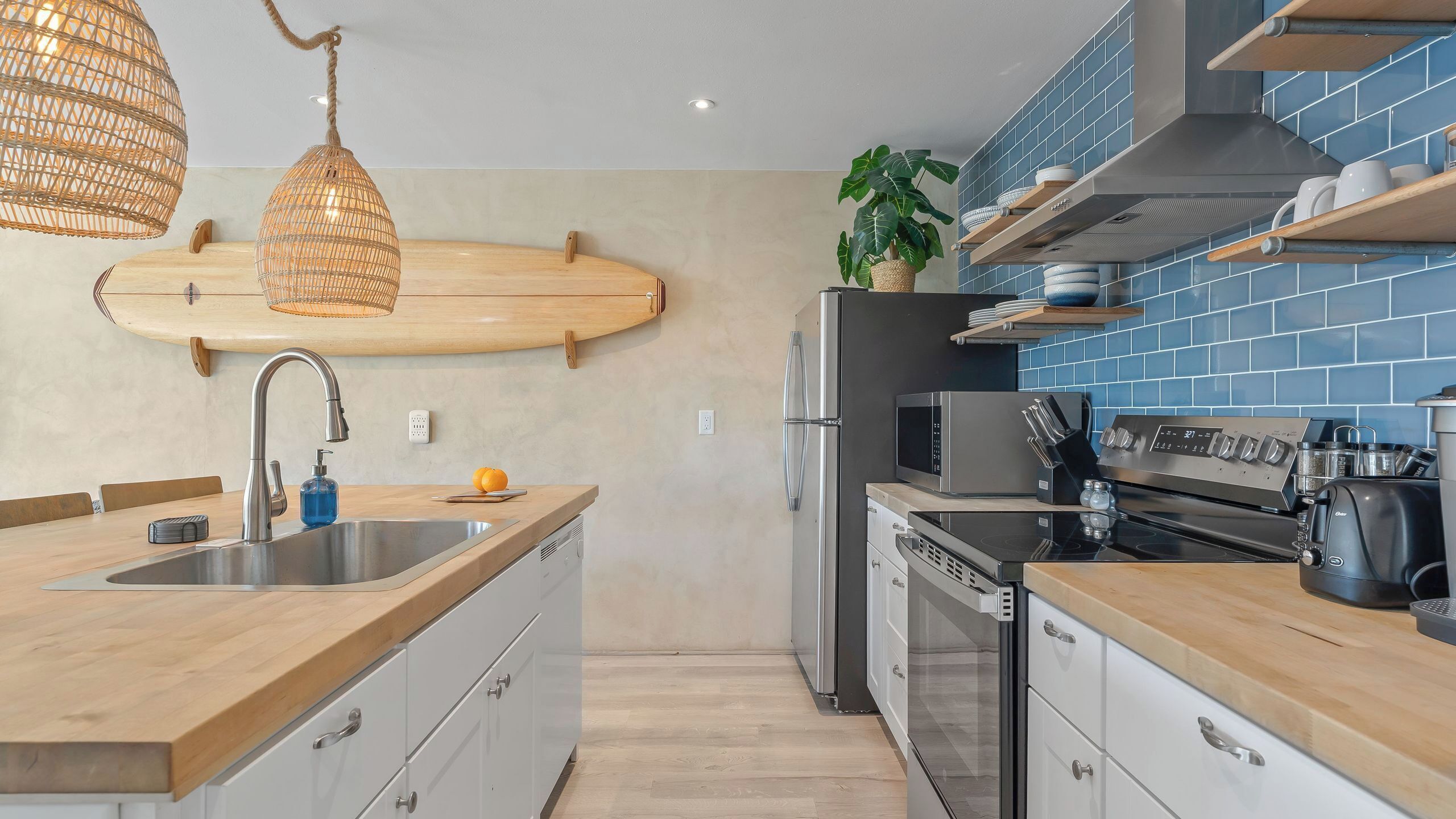 Une cuisine moderne avec un plan de travail en bois, des appareils électroménagers en acier inoxydable et un dosseret de carrelage bleu.