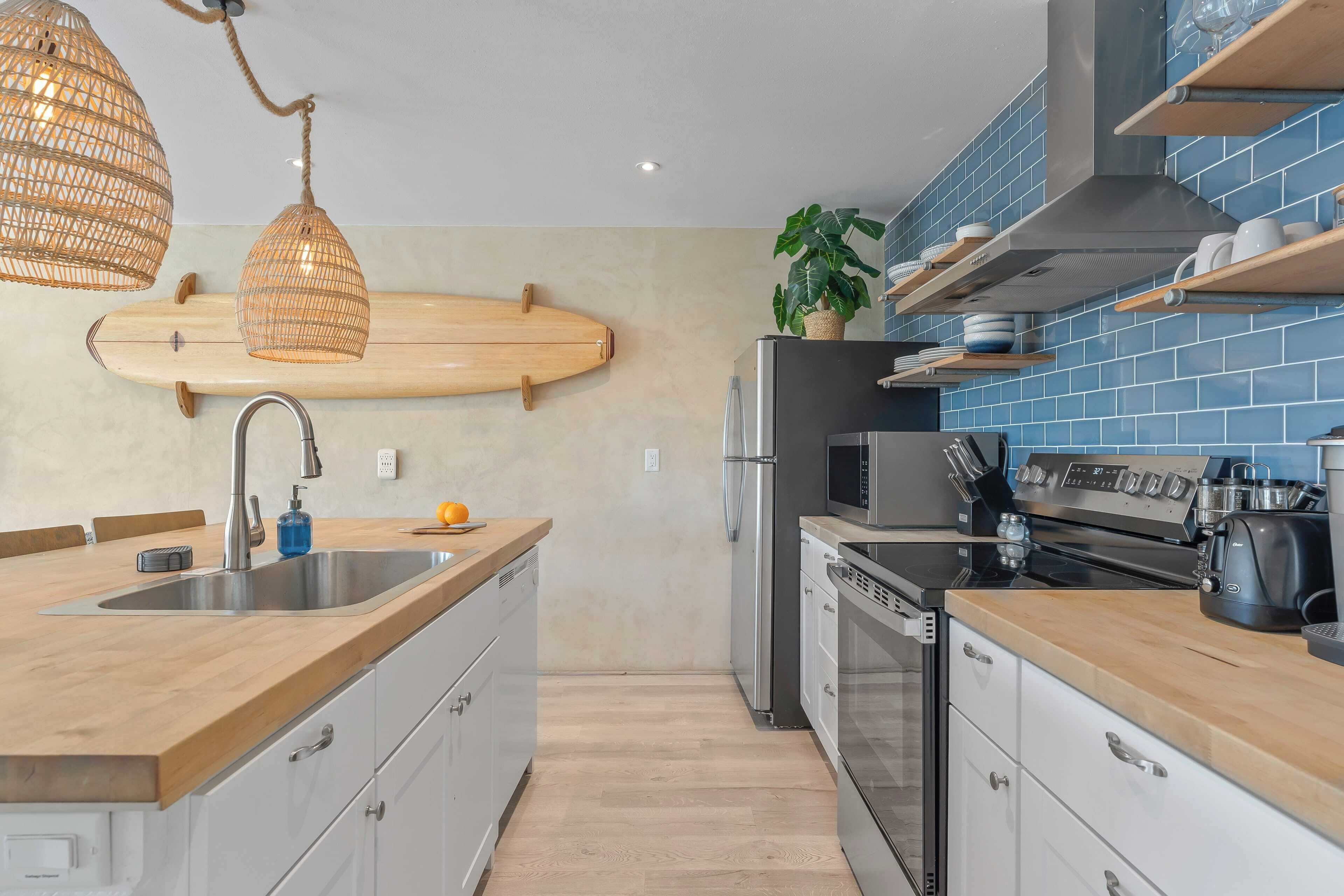 A modern kitchen with a wooden countertop, stainless steel appliances, and a surfboard mounted on the wall.
