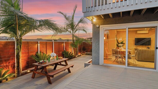 A patio with a wooden table and chairs, a wooden deck, and a view of the sunset. - Walk to Trestles Beach, Shared Yard+firepit El Camino Surfhouse A by Avantstay (San Clemente)
