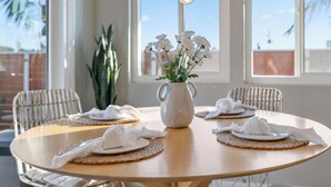 A round dining table with white placemats, a white pitcher with flowers, and wicker chairs. - Walk to Trestles Beach, Shared Yard+firepit El Camino Surfhouse A by Avantstay (San Clemente)