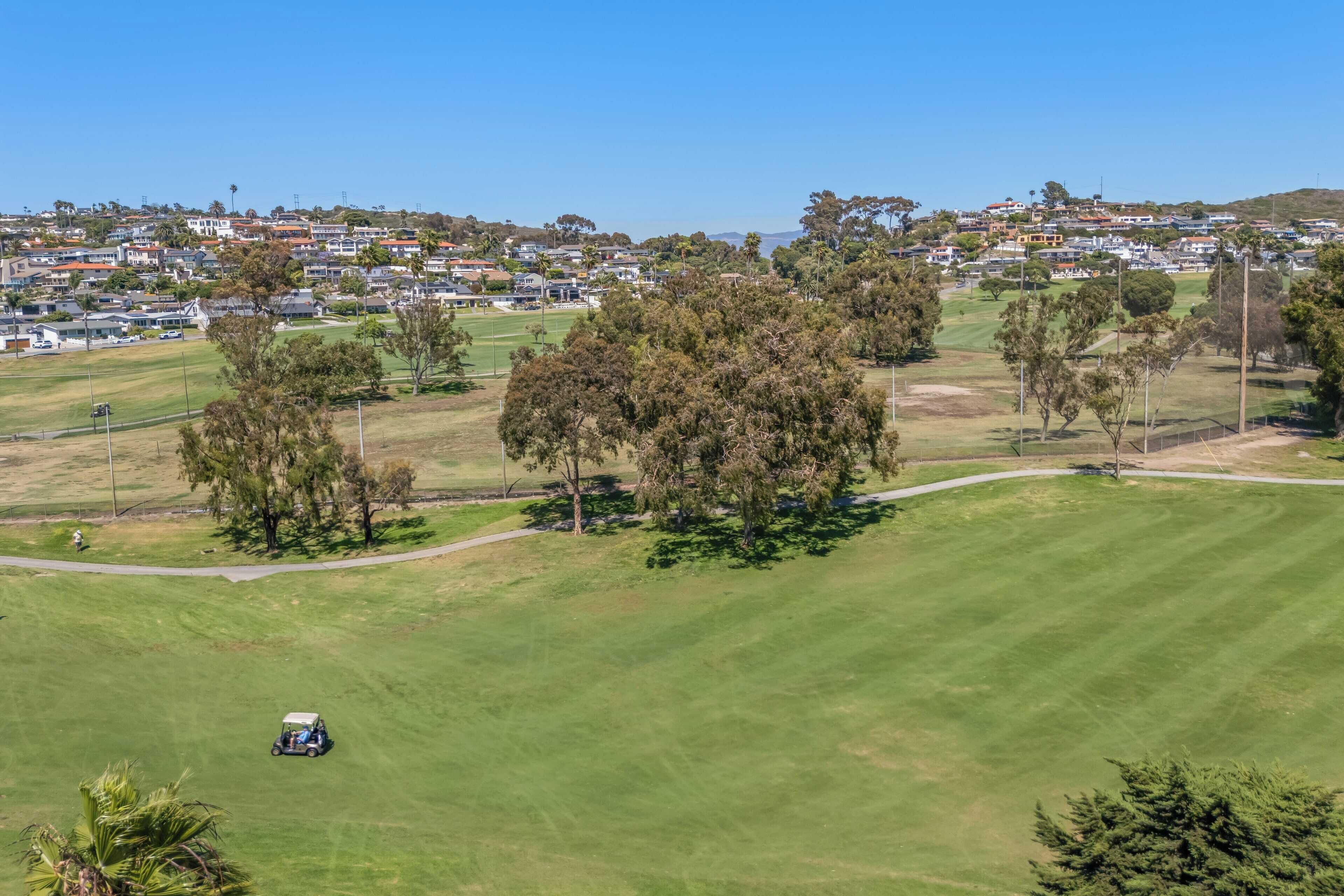 A golf course with a clear view of the surrounding residential area and a golf cart in the foreground.