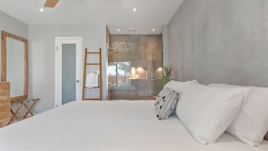 A bedroom with a large bed, a wooden ladder, a door, and a view into a bathroom with a shower and a sink. - Walk to Trestles Beach, Shared Yard+firepit El Camino Surfhouse A by Avantstay (San Clemente)