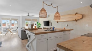 A modern kitchen with a wooden countertop, white cabinets, and a wooden surfboard mounted on the wall. - Walk to Trestles Beach, Shared Yard+firepit El Camino Surfhouse A by Avantstay (San Clemente)