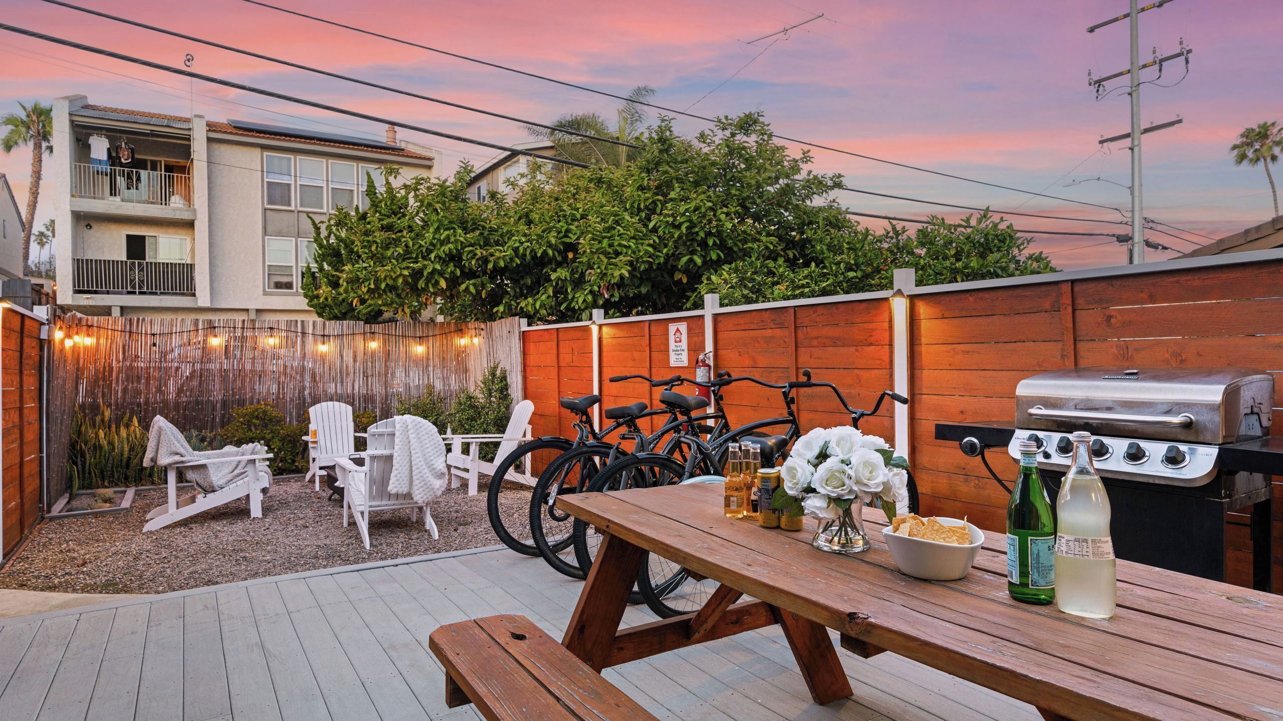 Un giardino sul retro con una griglia per barbecue, biciclette, mobili da patio e una recinzione in legno.
