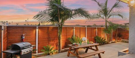 A backyard with a barbecue grill, wooden picnic table, and palm trees.