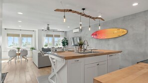 A modern kitchen with a central island, pendant lighting, and a surfboard decoration.