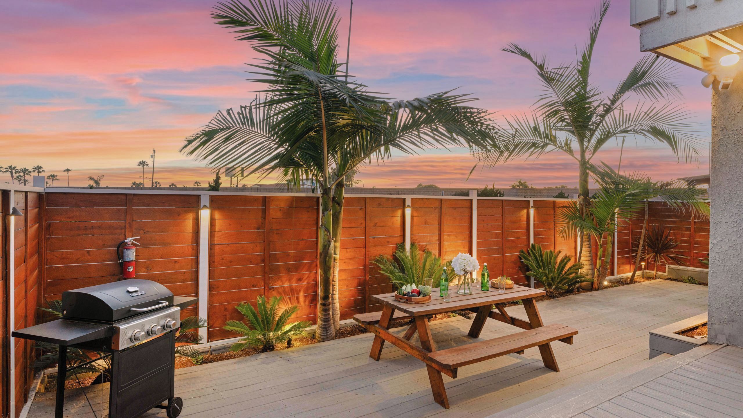 A patio with a grill, picnic table, and wooden fence.
