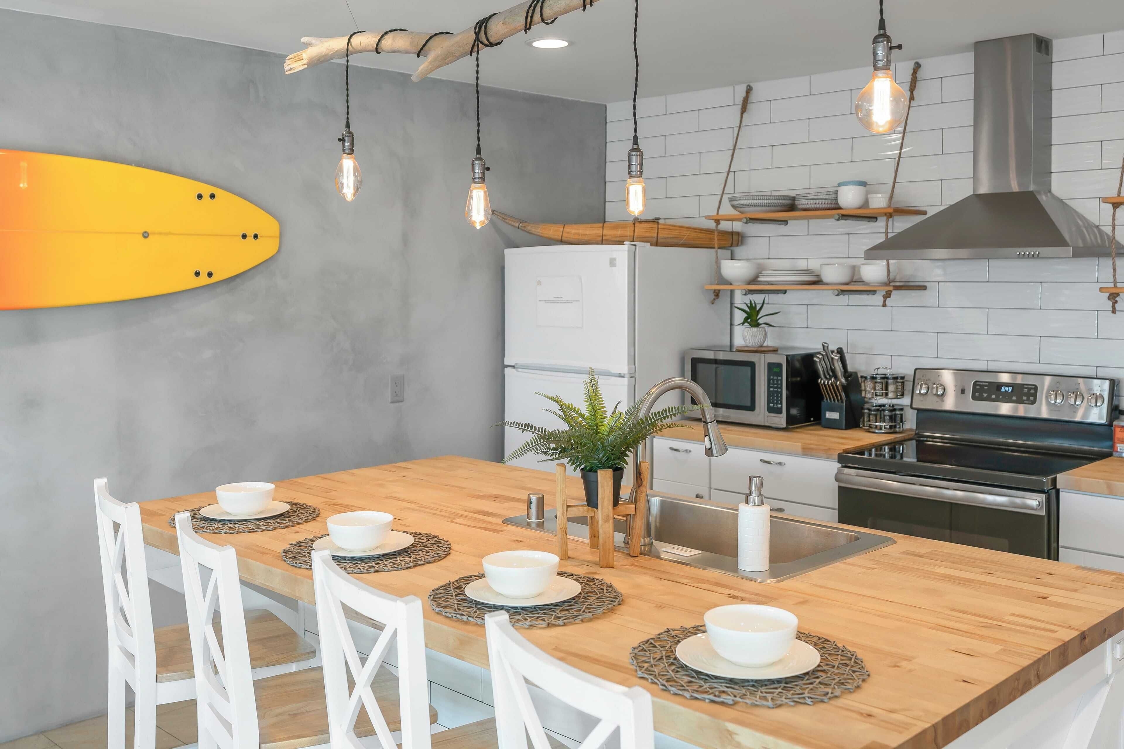 Una cocina moderna con una isla de madera, sillas blancas y un adorno con forma de tabla de surf.