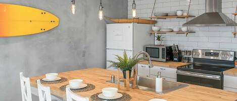 Una cocina moderna con una isla de madera, sillas blancas y un adorno con forma de tabla de surf.