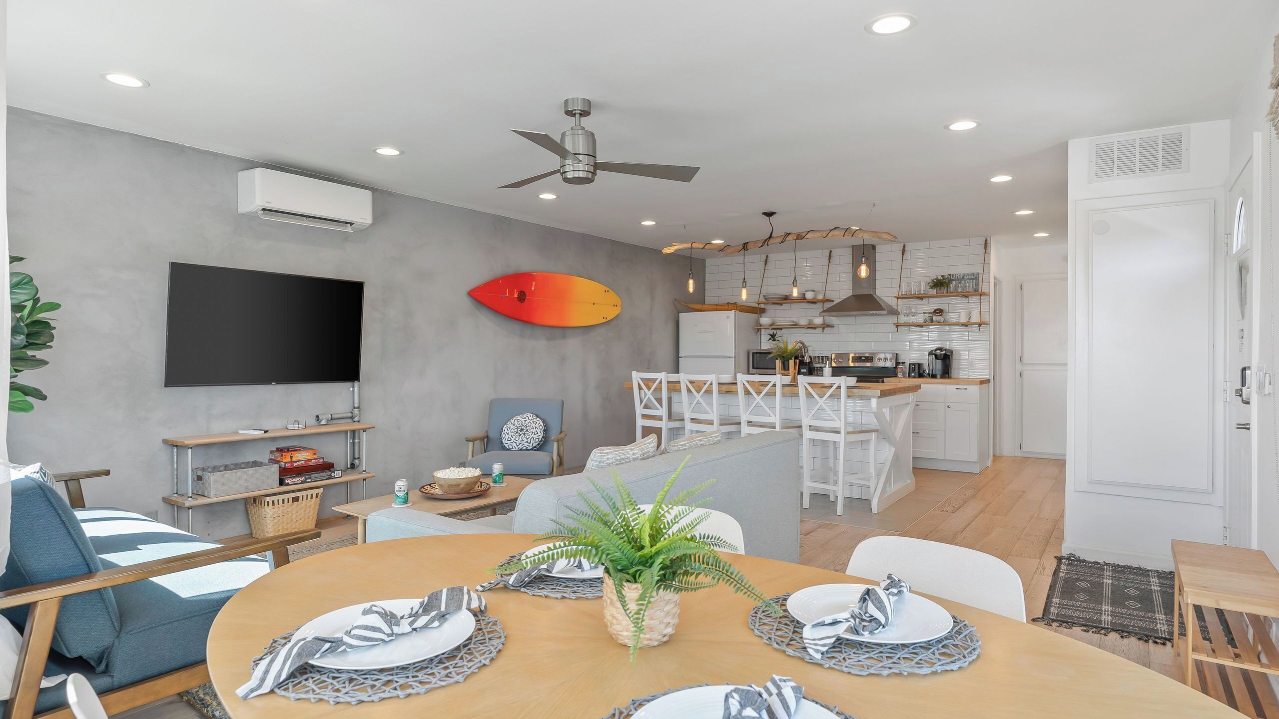 A modern living room with a dining area, kitchen, and a flat-screen TV mounted on the wall.