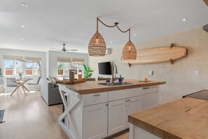 A modern kitchen with a wooden countertop, white cabinets, and a wooden surfboard mounted on the wall. - Walk to Trestles Beach Duplex w/ Ocean View El Camino Surfhouse by Avantstay (San Clemente)