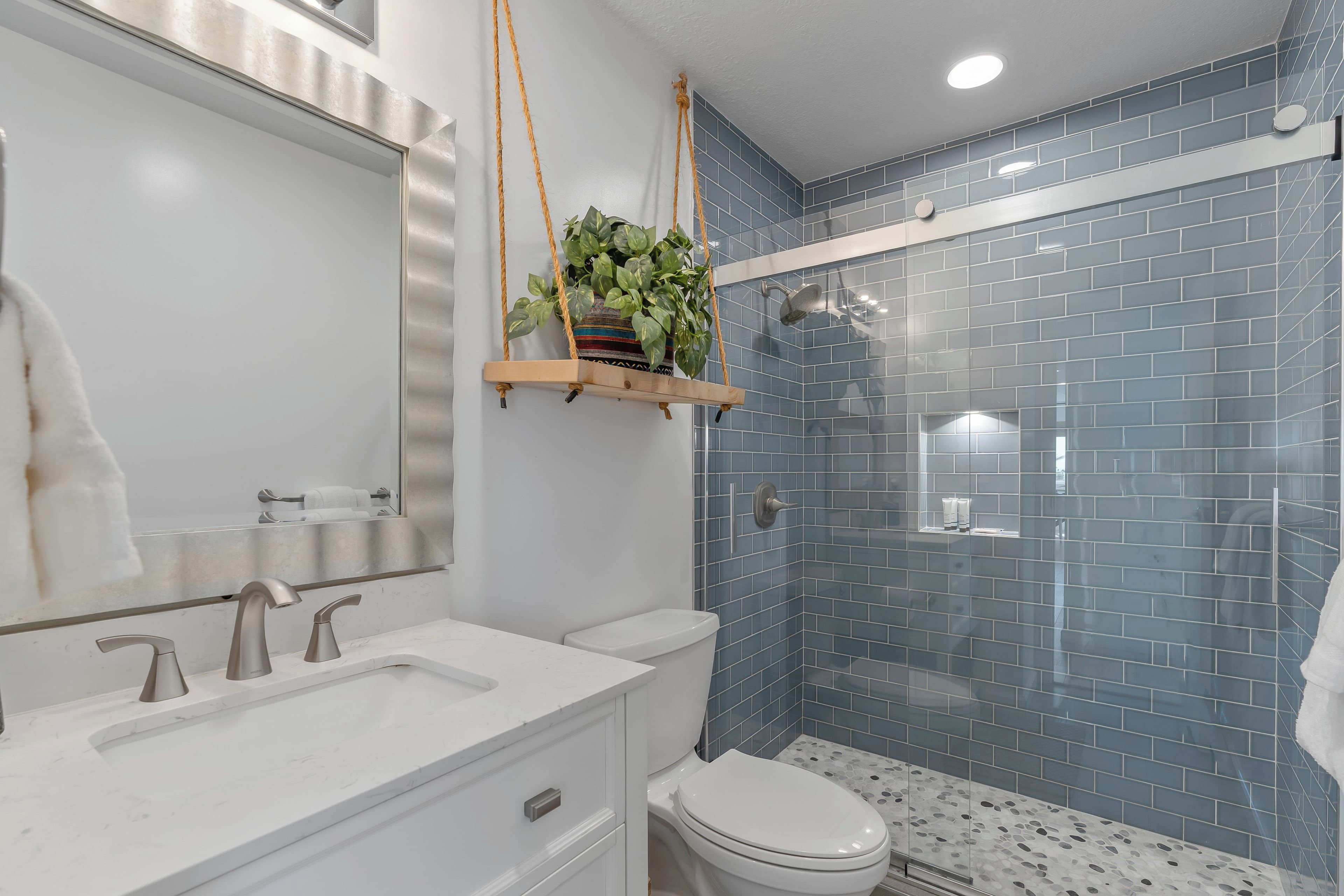 A modern bathroom with a white vanity, a hanging plant, and a glass shower enclosure.