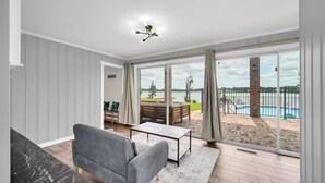 Ein geräumiges Wohnzimmer mit grauem Sofa, einem Couchtisch und Blick auf einen Swimmingpool und Außenbereich.
