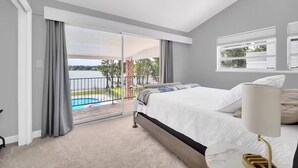 Ein Schlafzimmer mit einem großen Bett, Blick auf einen Swimmingpool und einem Balkon mit Geländer.