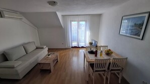 A modern living room with a sofa, coffee table, dining table with chairs, a TV, and a framed picture on the wall. - A apartment with balcony and the sea view (Seget Vranjica)