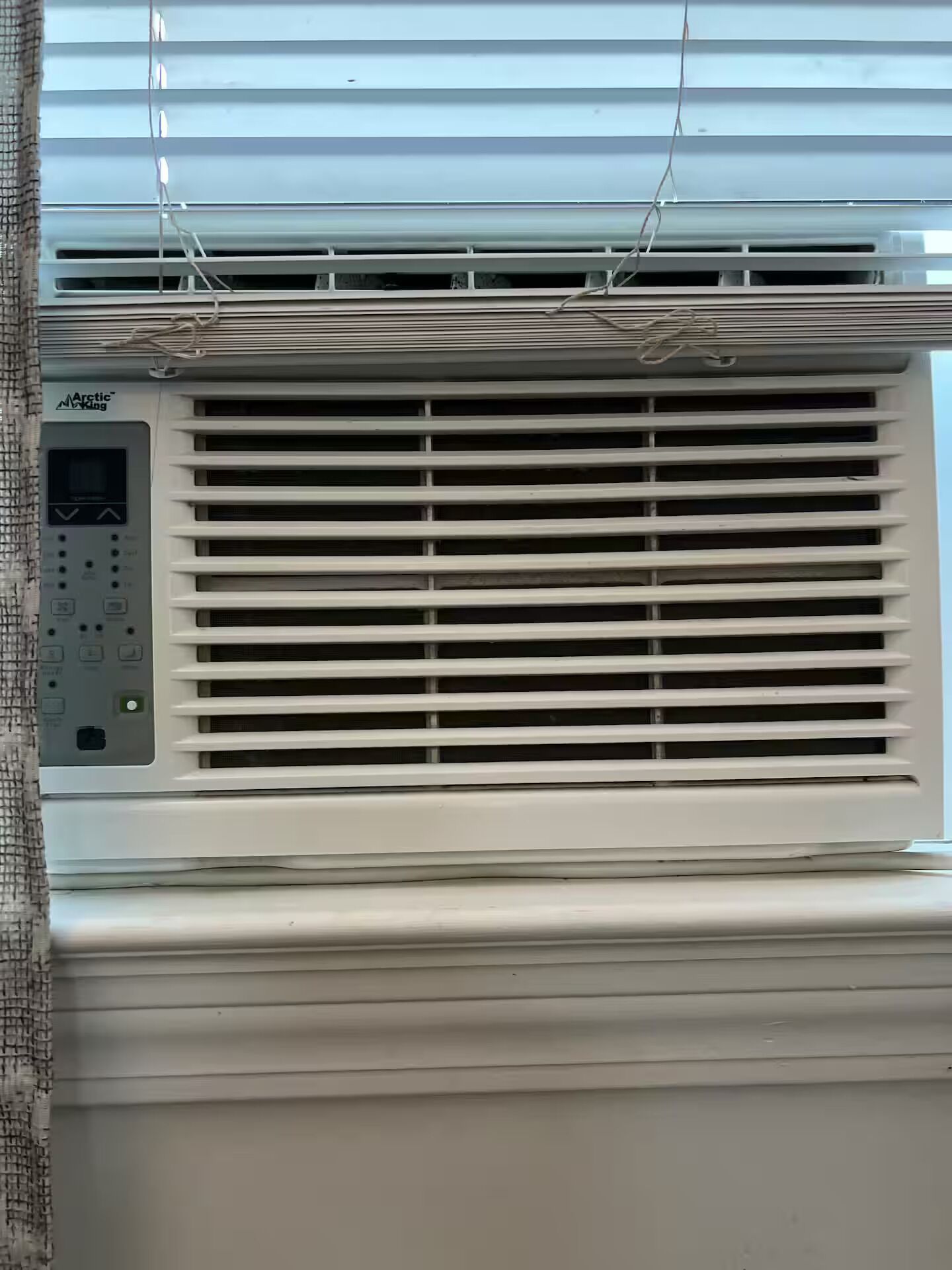 Un appareil de climatisation doté d’un panneau de commande et d’une fenêtre avec des stores.