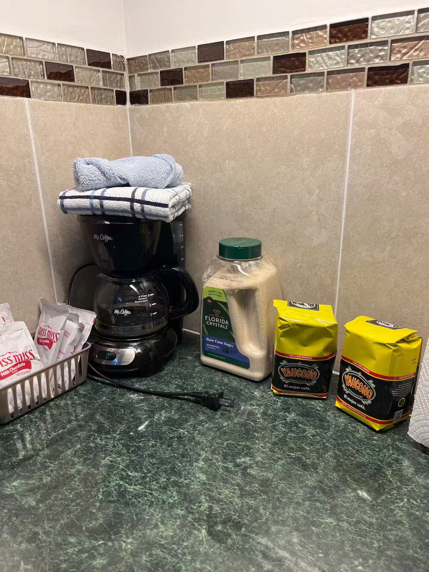 A kitchen area with a coffee maker, a bottle of raw cane sugar, and two bags of coffee.