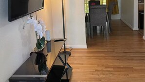 A modern living room with a flat-screen TV, a standing lamp, and a dining area with a table and chairs. - Apartamento con buen confort (Jacksonville)