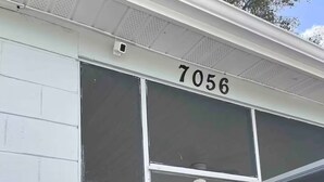 A building with the number 7056 on the facade, large glass windows, and a small porch with patterned chairs. - Apartamento con buen confort (Jacksonville)