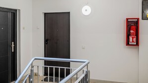 Un couloir avec une porte en bois sombre, un extincteur fixé au mur et une main courante en métal.