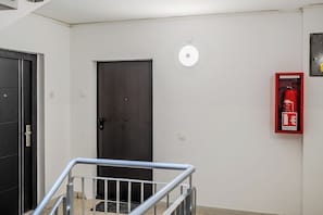 Un pasillo con una puerta oscura, un extintor y una lámpara en la pared.
