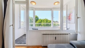 Une pièce avec une grande fenêtre, un radiateur et un canapé gris.