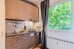 Cozinha moderna com armários de madeira, pia de aço inoxidável e janela com vista para árvores.