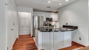 A modern kitchen with white cabinetry, a stainless steel refrigerator, a microwave, and a sink.
