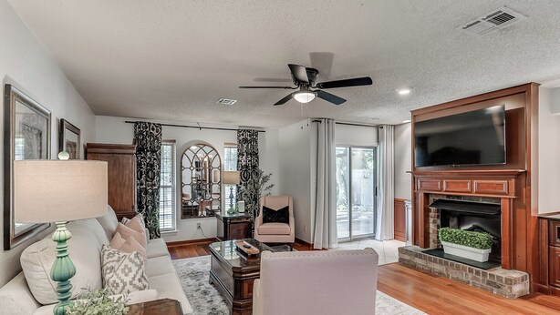 A living room with a fireplace, a ceiling fan, and a large flat-screen TV.