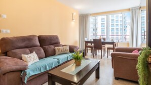 Una sala de estar con un sofá marrón, una mesa de centro de vidrio y una zona de comedor con mesa y sillas.