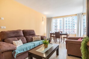 A living room with a brown sofa, a glass coffee table, and a dining area with a table and chairs.