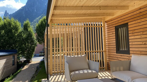 A wooden deck with outdoor seating, a view of mountains, and a building with a sloped roof. - Mountain View Lodge XL (1) - Idro (Idro)