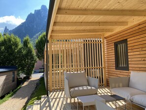 A wooden deck with outdoor seating, a view of mountains, and a building with a window. - Mountain View Lodge XL (1) - Idro (Idro)