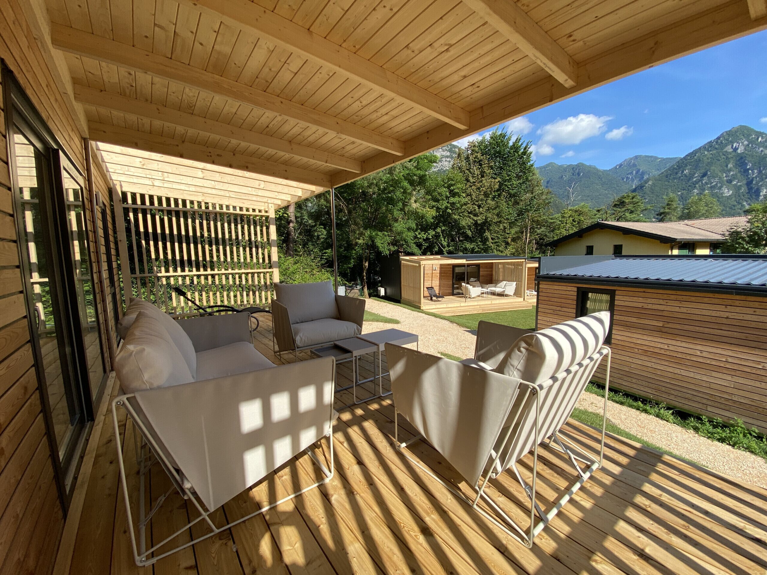 Un espacio de estar al aire libre cubierto, con suelo de madera, una pérgola de madera y vistas a un paisaje montañoso.