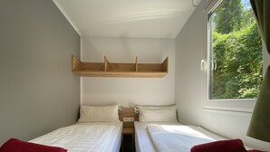 A room with two beds, a wooden shelf above the beds, and a window with a view of greenery. - Mountain View Lodge XL (1) - Idro (Idro)