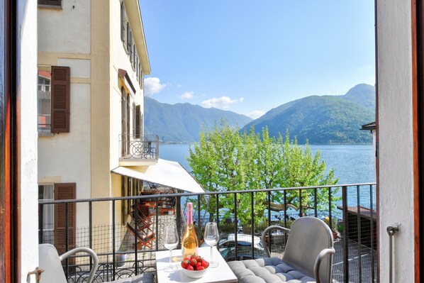 A balcony with a table, chairs, a bottle of wine, and a bowl of strawberries.