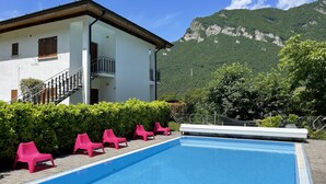A swimming pool with pink chairs, a white building with a balcony, and a mountainous backdrop.