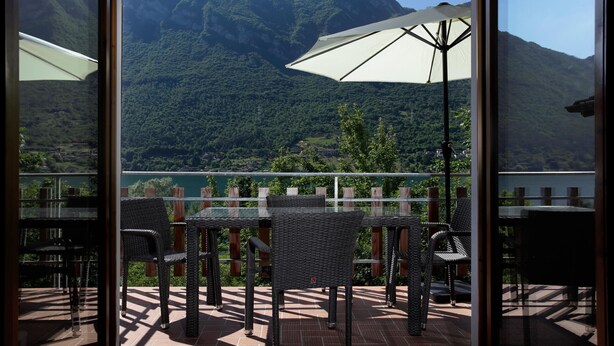 A terrace with wicker furniture and a table, overlooking a mountainous landscape.