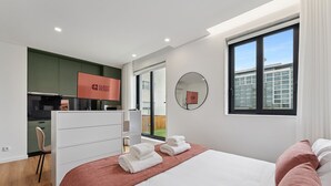 Una habitación de hotel moderna con una cama, un escritorio, una silla y vistas de la ciudad a través de amplias ventanas.