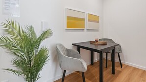 A small dining area with a table and two chairs, a potted plant, and two framed artworks on the wall.