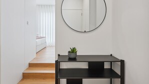 A modern interior with a staircase leading to a bedroom, a round mirror on the wall, and a small table with a plant.