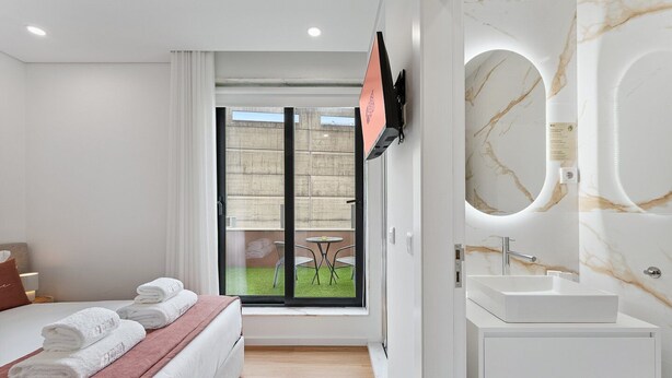 A modern bedroom with a bed, a large window, a TV, and a bathroom with a marble sink and mirror.