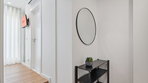 A modern hallway with a black metal shelf holding a plant, white walls, and a door with a screen.
