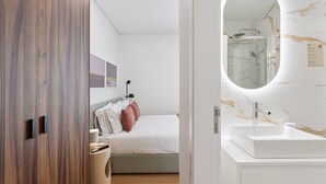 Une chambre à coucher moderne avec un lit, une lampe de chevet et une salle de bain équipée d’un lavabo et d’un miroir.