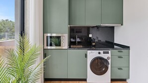 Une cuisine compacte équipée d’un lave-linge et d’un sèche-linge intégrés, d’un four à micro-ondes et d’un petit plan de travail avec un évier et une plaque de cuisson.