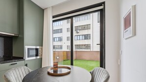 A modern kitchen with a round dining table and two chairs, a microwave, and a view of a building and green space through a sliding door. - GuestReady - Tutti Frutti Studio - Cherry (Porto)