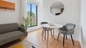 Ein modernes Wohnzimmer mit einem grauen Sofa, einem runden Tisch mit Stühlen, einem Blumentopf und einem großen Fenster mit Aussicht.